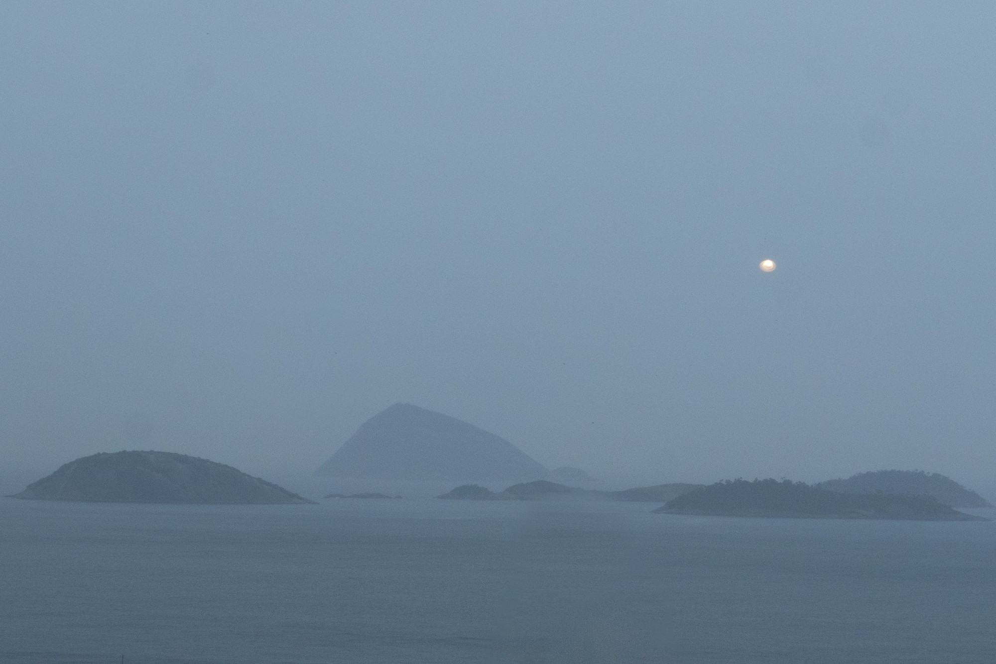 A full moon rises over fog-shrouded islands in Guanabara Bay, Rio de Janeiro.
