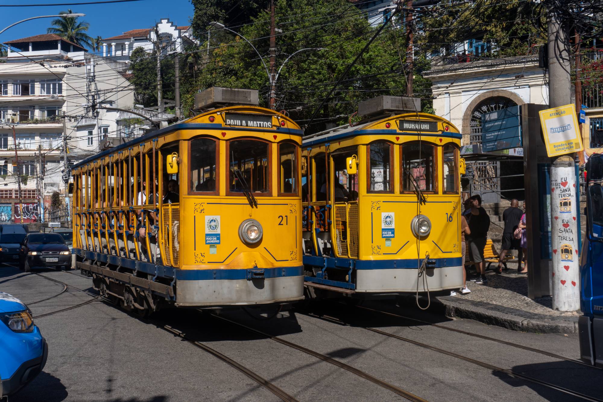 Two yellow trams meet on the tracks in Santa Teresa, Rio de Janeiro, passengers and pedestrians filling the street.